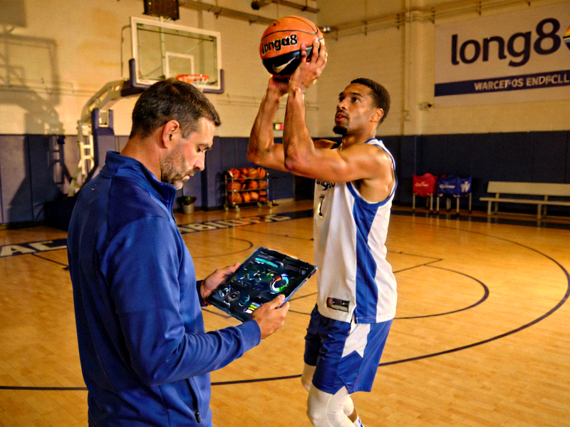 专业篮球运动员在训练馆内使用long8智能篮球进行投篮训练，教练通过平板电脑查看实时数据